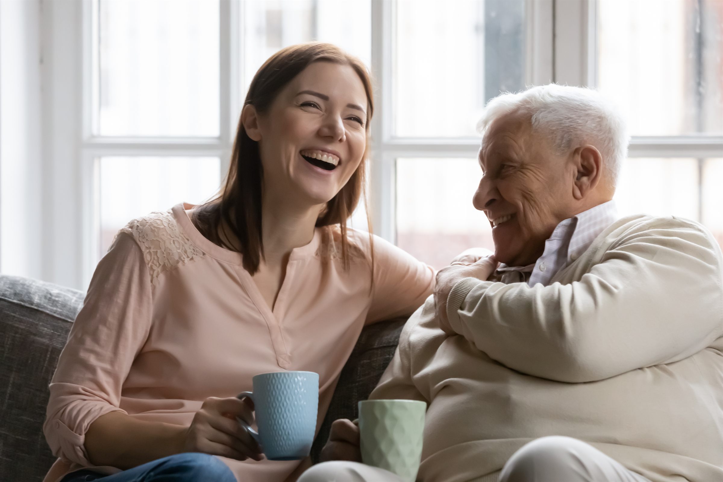 Young woman laughing with elderly man over coffee